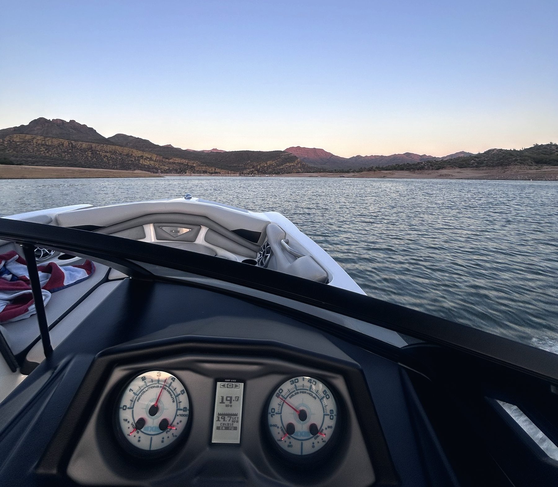 View over the dash of a wake boat cruising across a lake at dusk